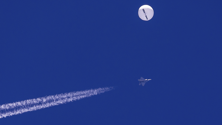 A large balloon drifts above the Atlantic Ocean, just off the coast of South Carolina, with a fighter jet and its contrail seen below it Saturday. (Chad Fish via AP)